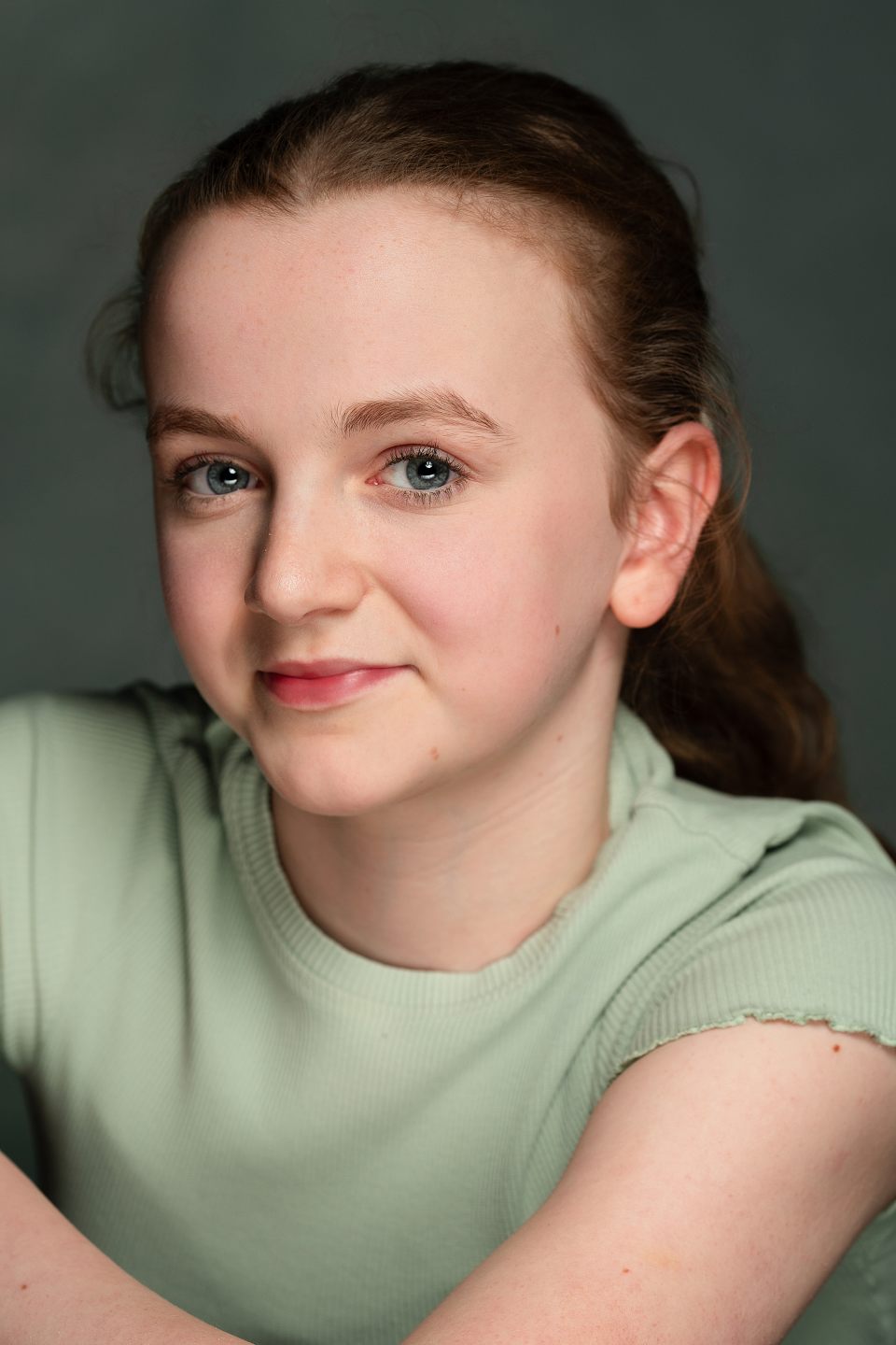 Close-up portrait of a girl with blue eyes and light brown hair wearing a mint-green top, looking at the camera with a soft smile.